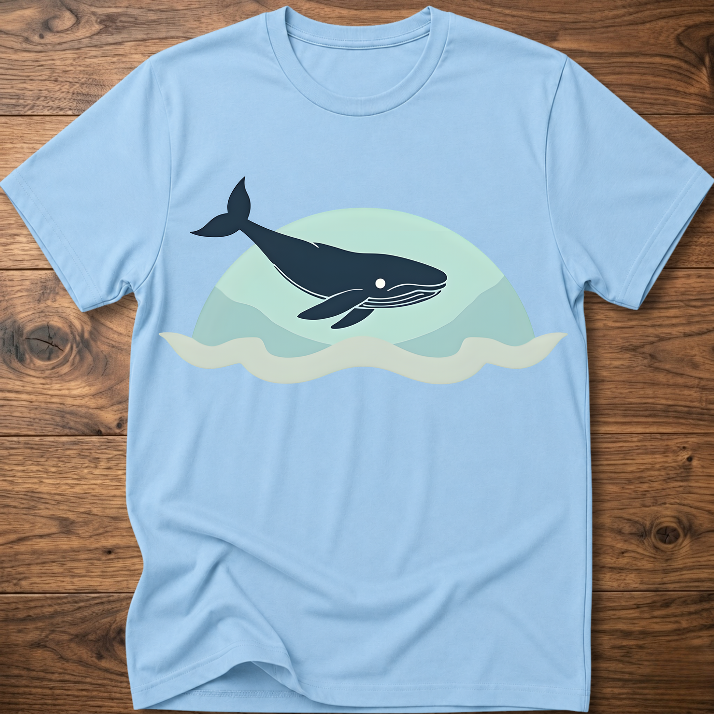 Light blue crew-neck t-shirt with dark whale graphic over teal waves design