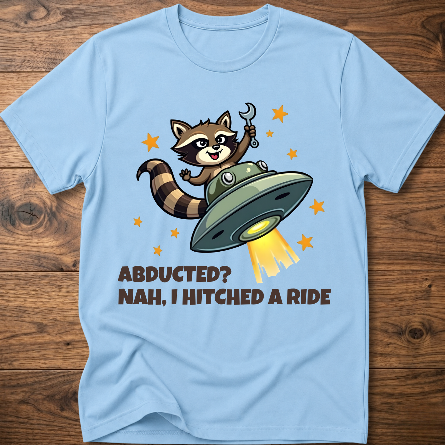 Powder blue raccoon UFO graphic T-shirt with 'ABDUCTED?' and 'HITCHED A RIDE' text
