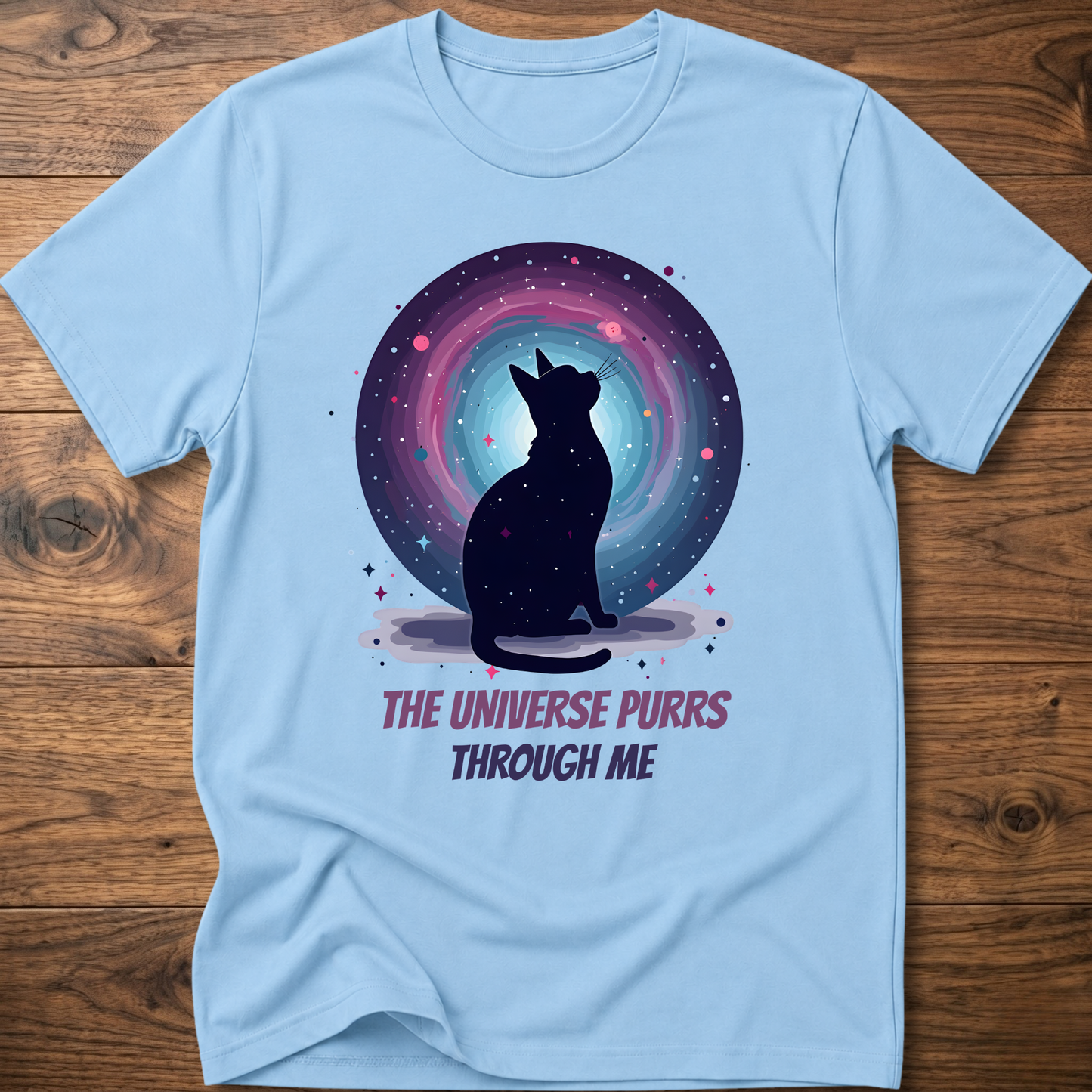 Light blue cat t-shirt with cosmic cat silhouette and purple "The universe purrs through me" text