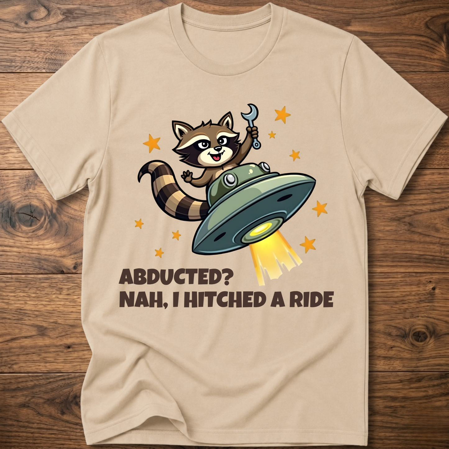 Sand beige raccoon UFO graphic T-shirt with 'ABDUCTED?' and 'HITCHED A RIDE' text