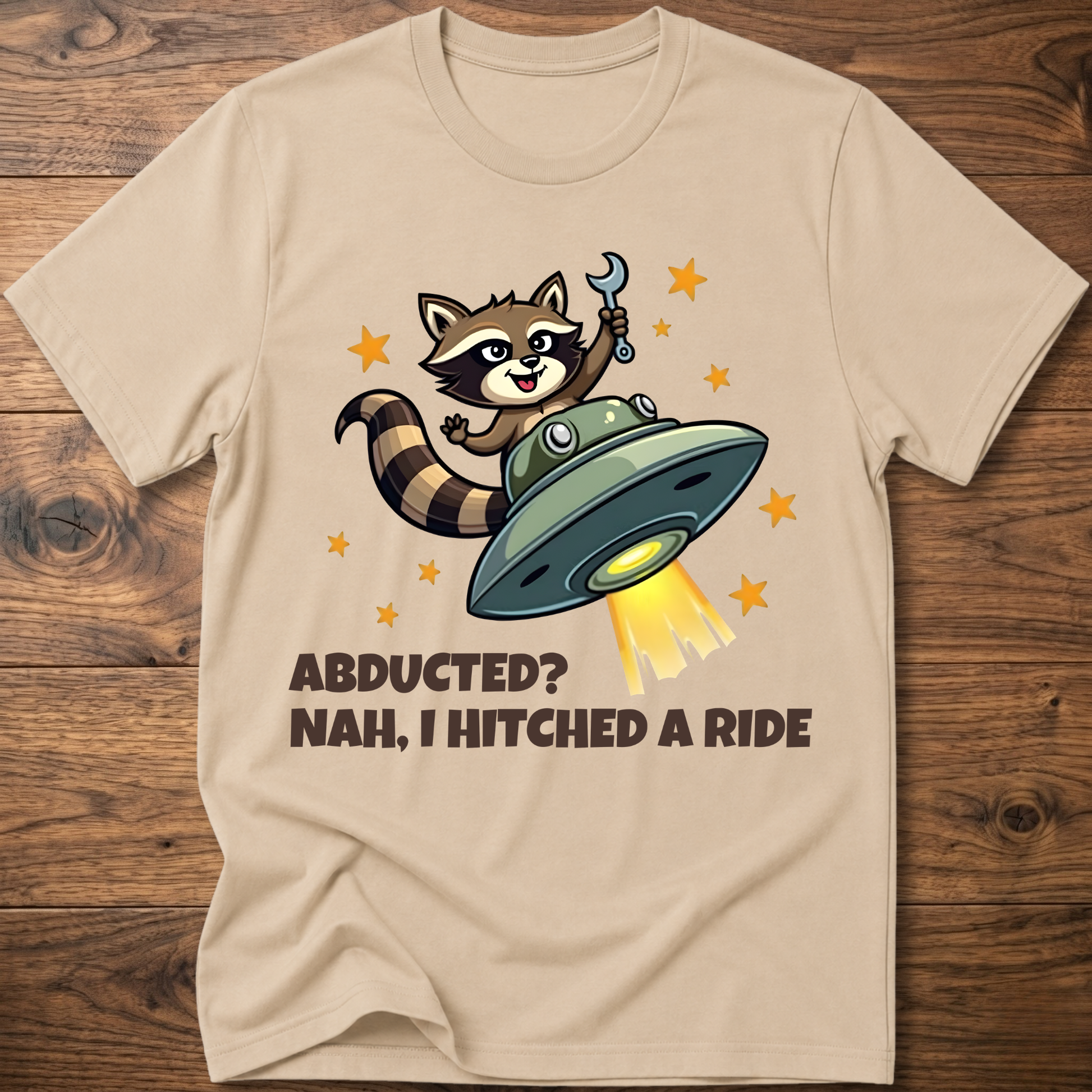 Sand beige raccoon UFO graphic T-shirt with 'ABDUCTED?' and 'HITCHED A RIDE' text